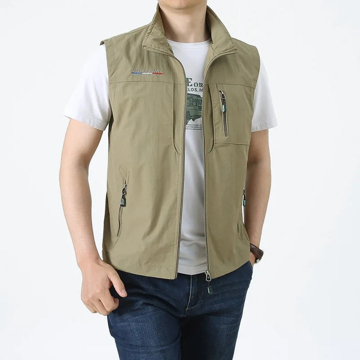 Mann trägt beige Outdoor-Weste mit Reißverschlusstaschen über weißem T-Shirt und blauer Jeans. Freizeitmode, Herrenbekleidung, Outdoor-Stil.