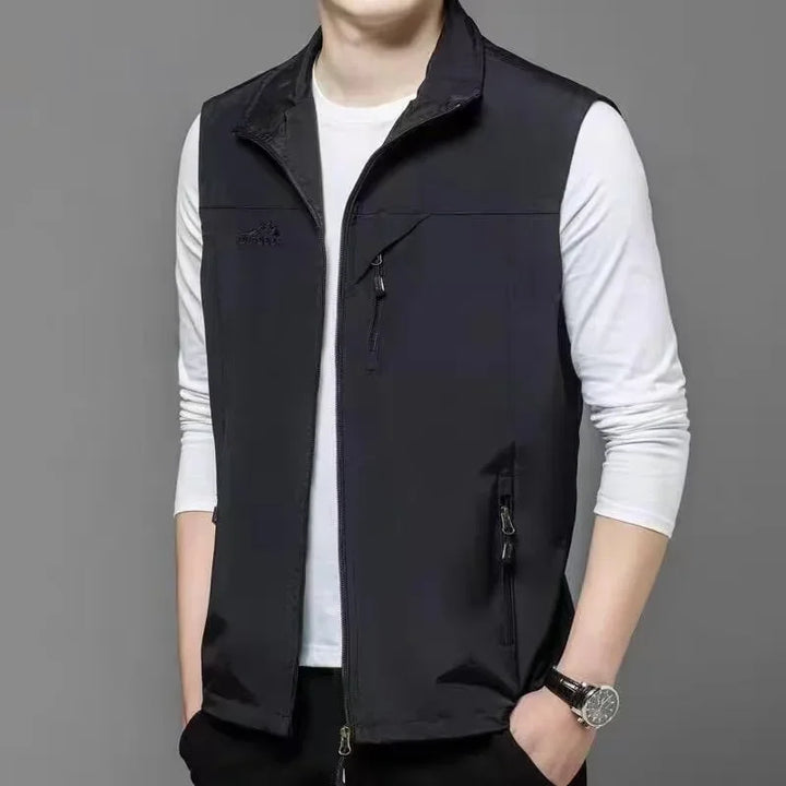 Schwarze Herrenweste mit Reißverschluss über weißem Langarmshirt, grauer Hintergrund. Modische Freizeitkleidung, ideal für Herbst und Frühling.