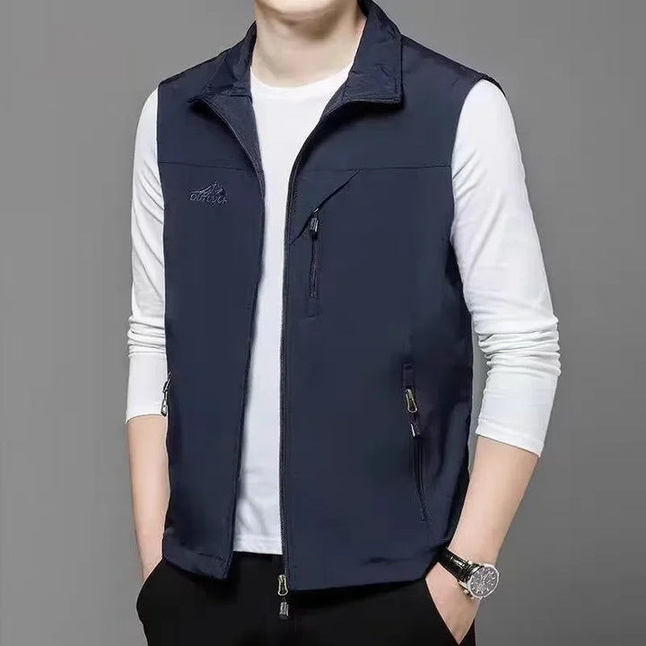 Mann trägt dunkelblaue Weste über weißem Langarmshirt, grauer Hintergrund. Modische Herrenbekleidung, Freizeitlook, stilvolle Weste.