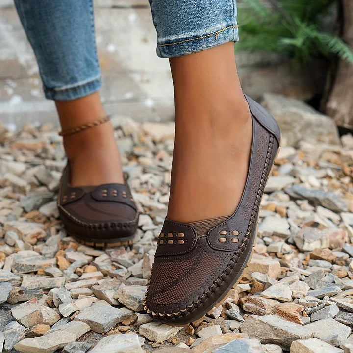 Braune Damen-Loafer aus Leder auf Kiesweg, getragen mit blauen Jeans. Bequeme, stilvolle Schuhe für Freizeit und Alltag.