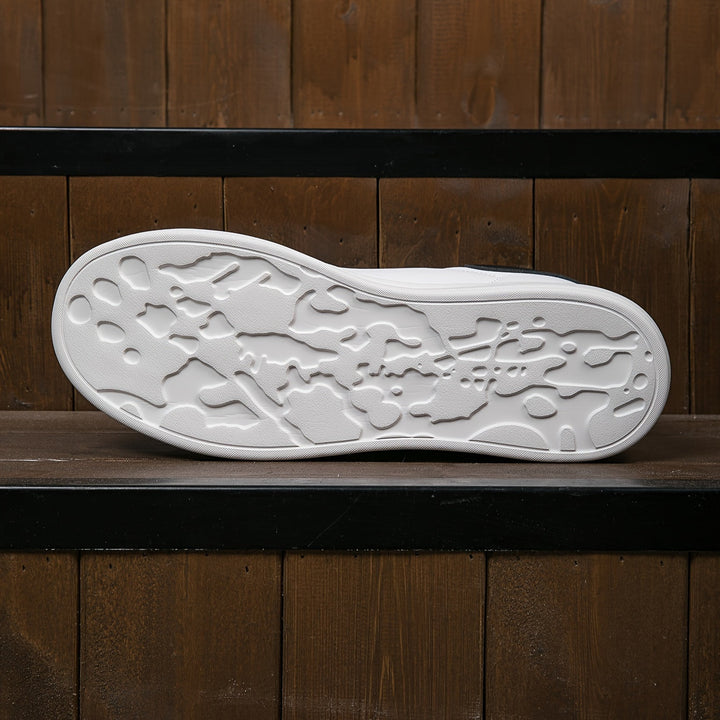Weiße Sneaker-Sohle mit strukturiertem Profil auf dunklem Holzuntergrund. Moderne Schuhsohle, rutschfest, ideal für urbanen Stil.