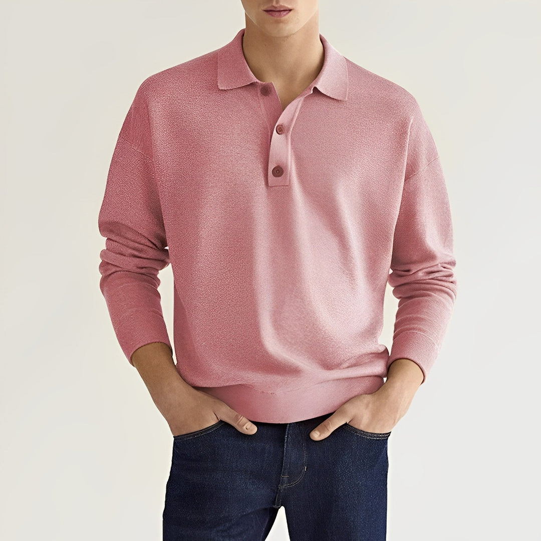 Junger Mann in rosa Polo-Pullover und blauer Jeans vor neutralem Hintergrund. Modetrend, Herrenbekleidung, lässiger Stil.