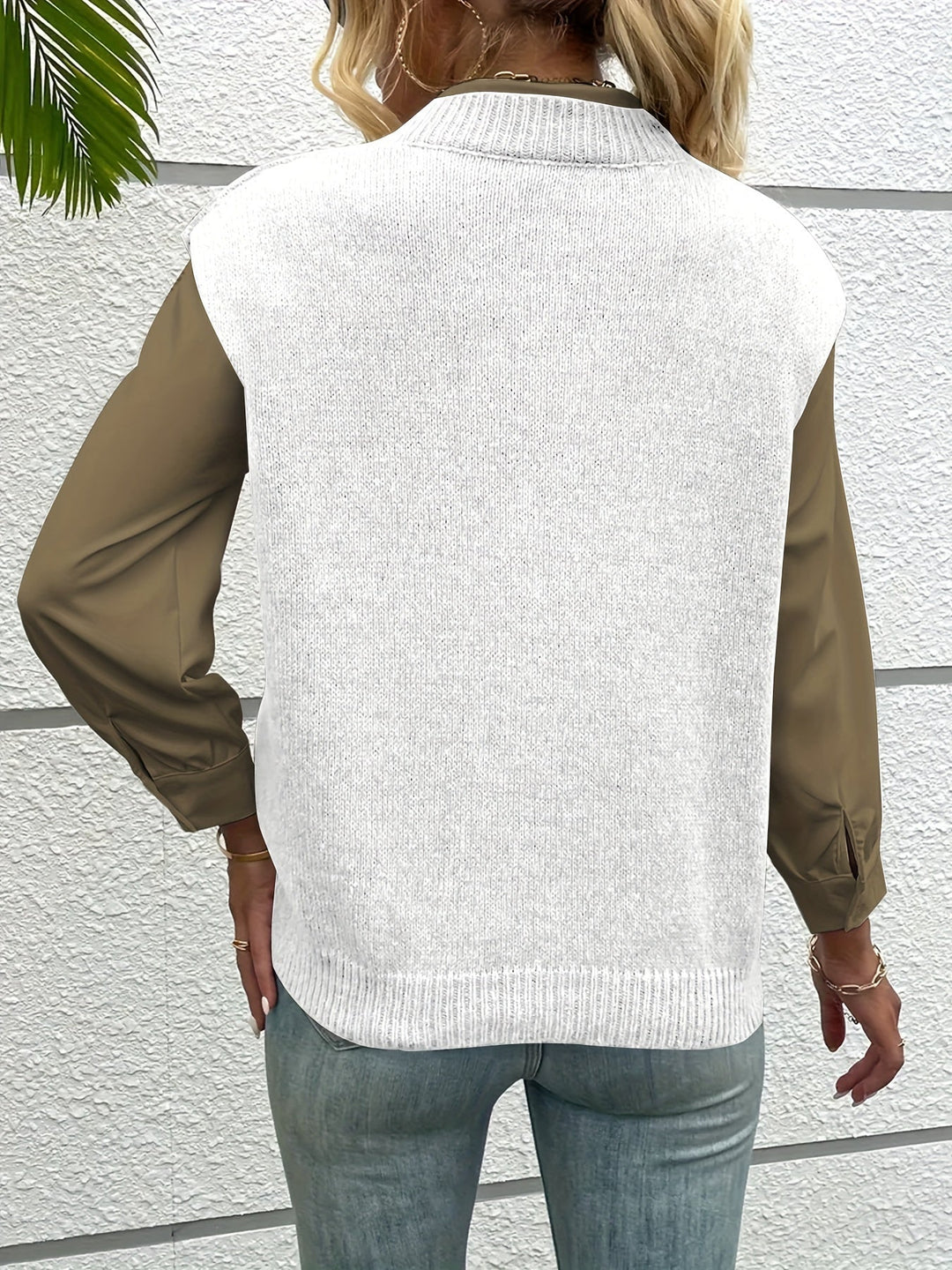Frau in weißem Strickpullover und olivgrüner Bluse, Rückansicht, vor weißer Wand. Modetrend, Herbstmode, lässiger Stil.