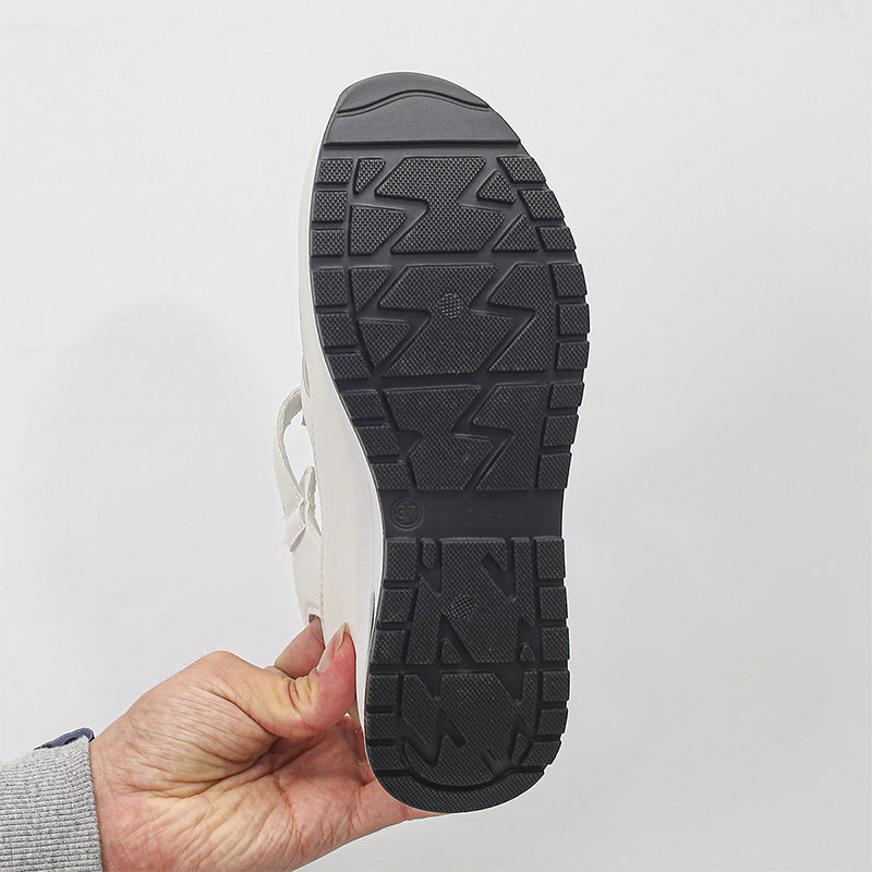 Hand hält weißen Sneaker mit schwarzer, rutschfester Sohle. Modischer Freizeitschuh, ideal für Alltag und Sport. Hochwertige Verarbeitung.