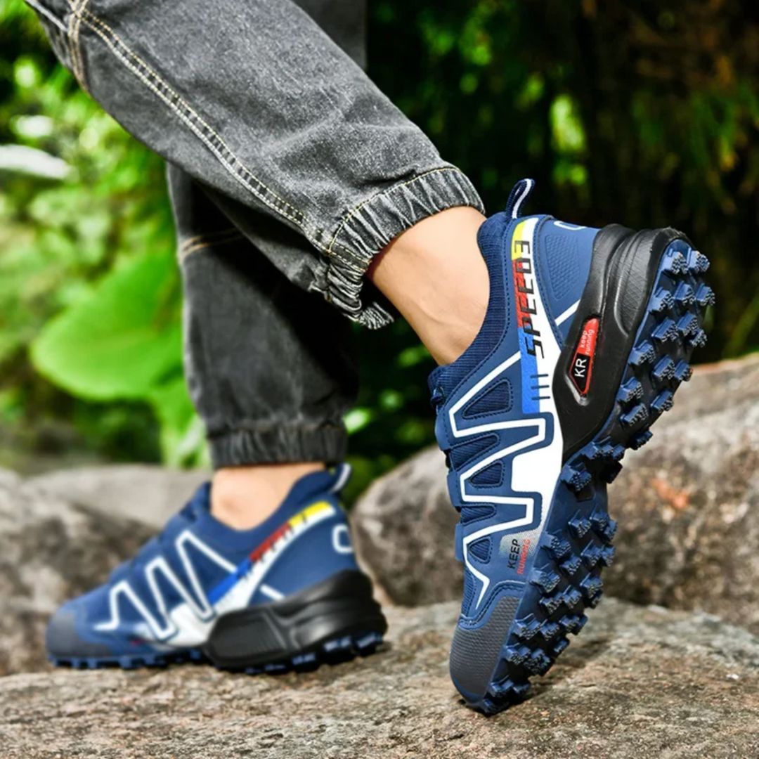 Blaue Trailrunning-Schuhe mit grobem Profil auf Felsen, getragen von Person in Jeans. Outdoor-Schuhe, ideal für Wandern und Laufen im Gelände.