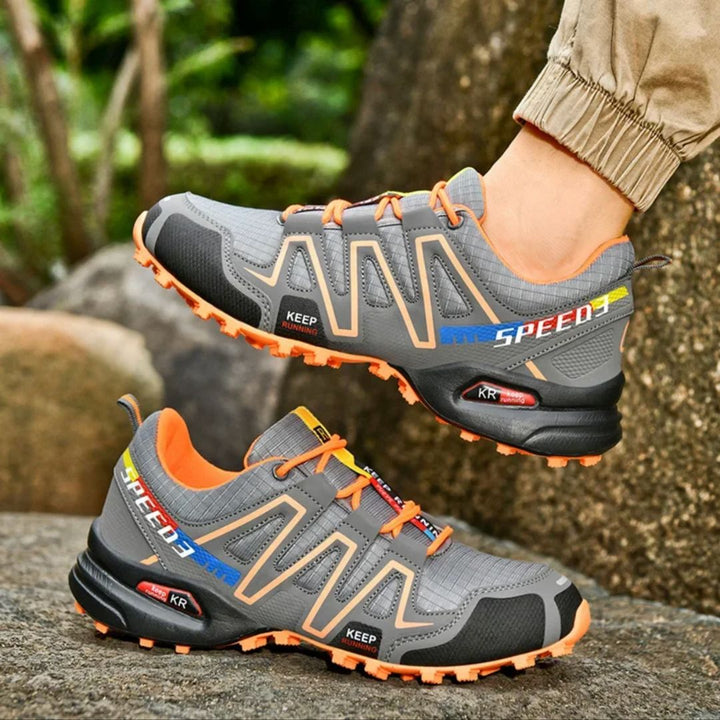 Graue Outdoor-Laufschuhe mit orangefarbenen Akzenten, robustem Profil und atmungsaktivem Mesh. Ideal für Trailrunning und Wandern.