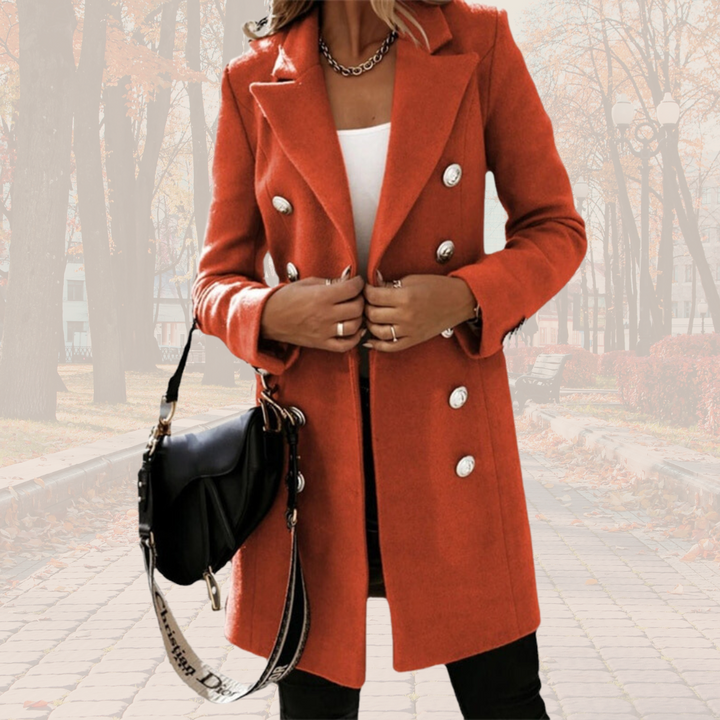 Frau in rotem Wollmantel mit doppelter Knopfleiste, weißem Top und schwarzer Umhängetasche, steht auf herbstlichem Gehweg. Elegante Herbstmode.