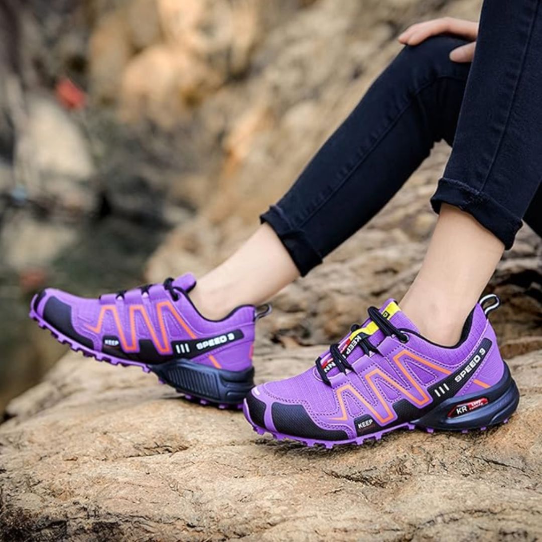 Lila Wanderschuhe auf Felsen, Damenbeine in schwarzen Jeans, Outdoor-Abenteuer, robuste Sohlen, modische Trekking-Schuhe, Naturerlebnis.