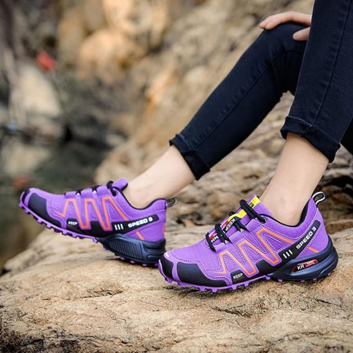 Lila Wanderschuhe auf Felsen, Damenbeine in schwarzen Jeans, Outdoor-Abenteuer, robuste Sohlen, modische Trekking-Schuhe, Naturerlebnis.