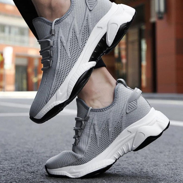 Graue Sportschuhe mit weißer Sohle auf Asphalt, modernes Design, atmungsaktives Material, ideal für Laufen und Fitness, urbaner Hintergrund.