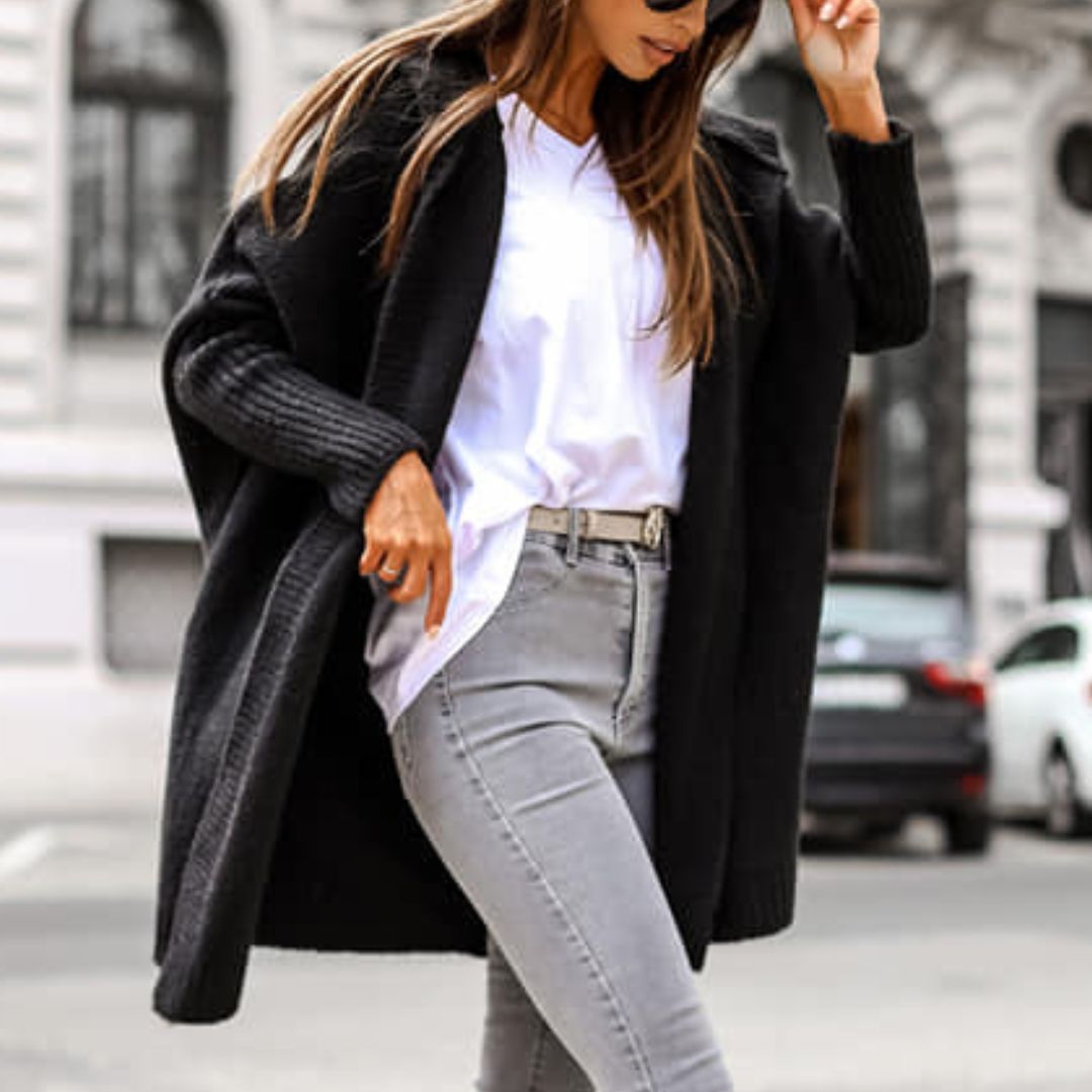 Frau in schwarzem Strick-Cardigan und weißem T-Shirt auf städtischer Straße. Modetrend, Herbstmode, lässiger Stil, Straßenmode.
