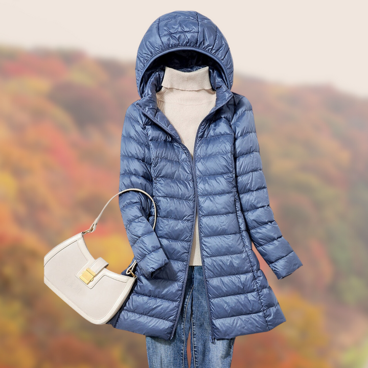 Blaue Daunenjacke mit Kapuze, kombiniert mit weißer Handtasche und Jeans, vor herbstlichem Hintergrund. Damenmode, Herbstoutfit, Outdoor-Bekleidung.