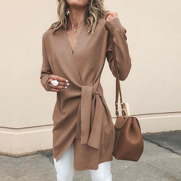 Frau in braunem Wickelcardigan mit Tasche, trägt weiße Hose. Modetrend Herbst, eleganter Damenlook, stilvolle Freizeitkleidung.