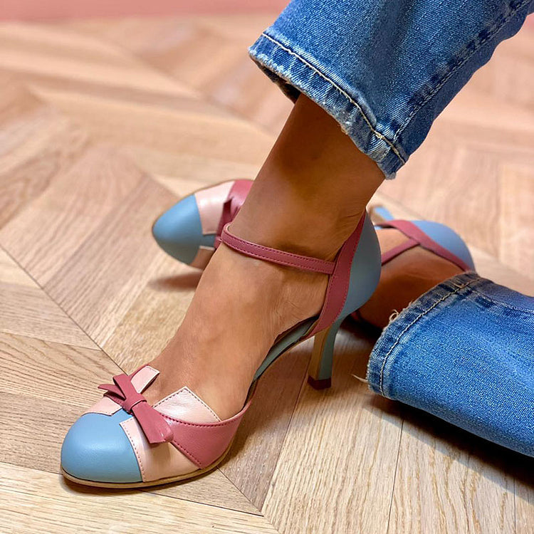 Frau trägt elegante, mehrfarbige High Heels mit Schleifen-Detail auf Parkettboden. Modische Damenschuhe, pastellfarben, stilvoll, Jeans.