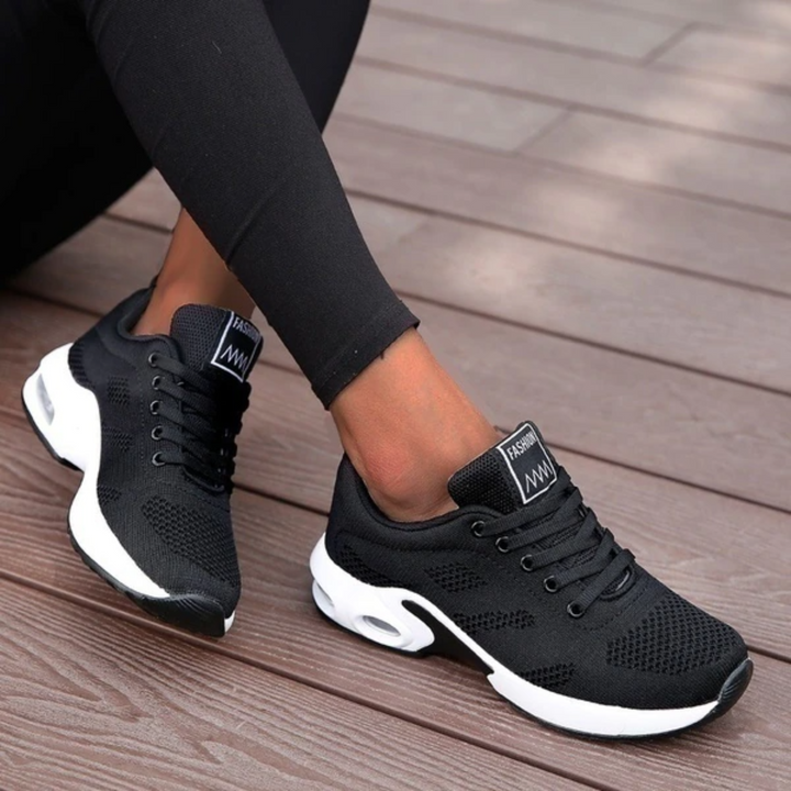 Schwarze Damen-Sneaker mit weißer Sohle auf Holzterrasse, modisch und bequem, ideal für Freizeit und Sport, atmungsaktives Material.