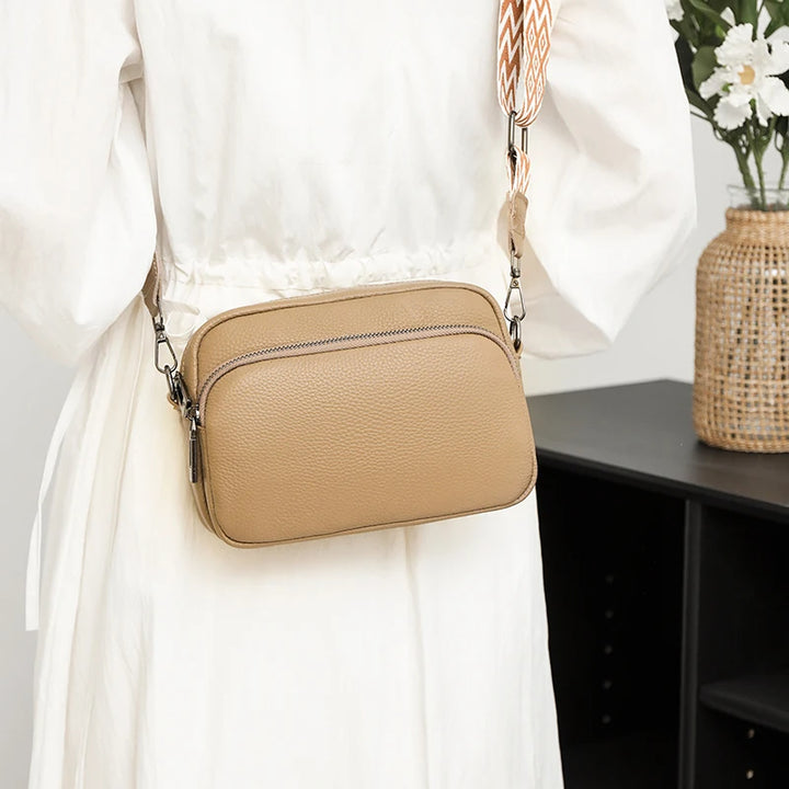 Beige Umhängetasche aus Leder an Frau in weißem Kleid, modisches Accessoire, elegantes Design, ideal für Alltag und Freizeit.