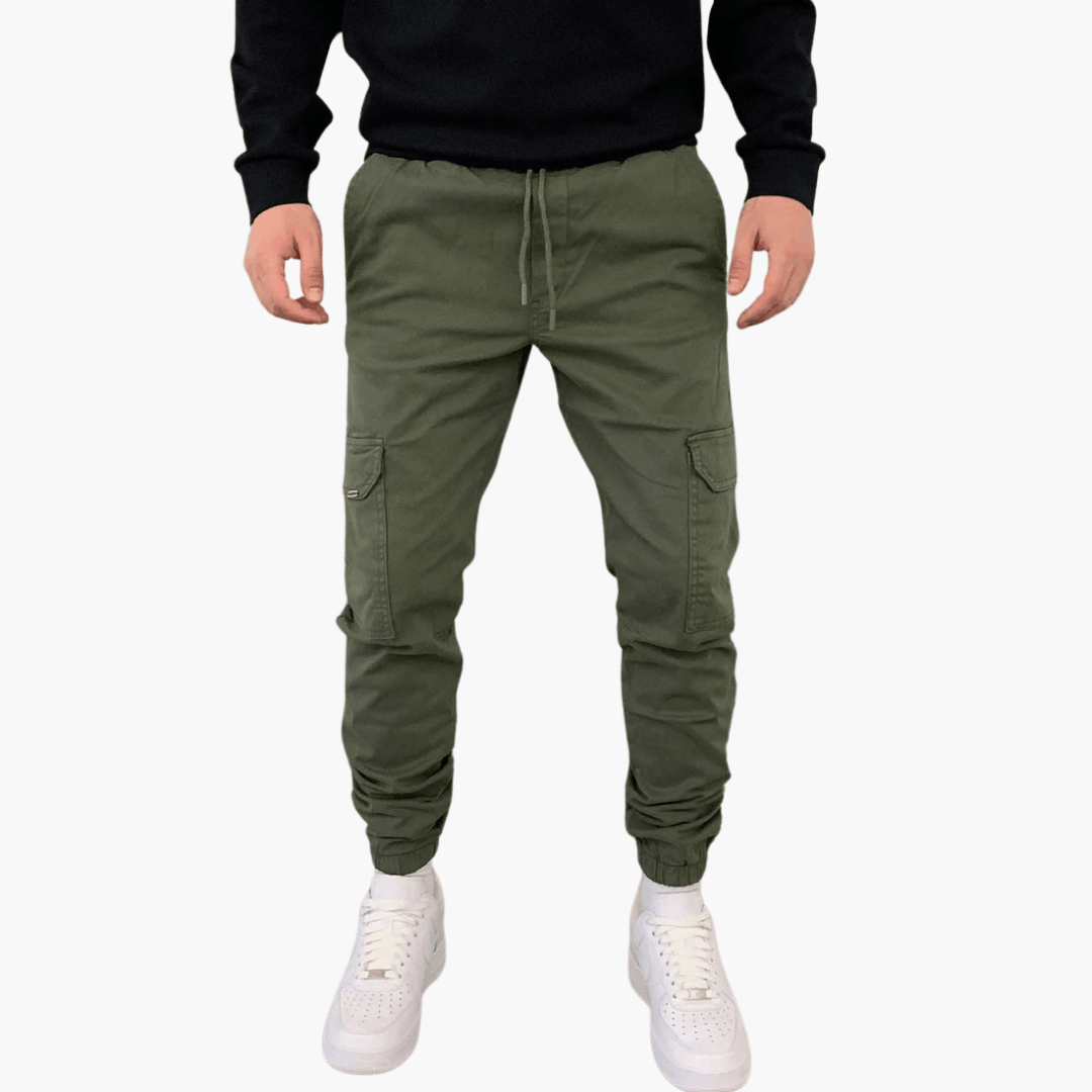 Grüne Cargo-Jogginghose für Herren, lässiger Stil, mit Taschen, kombiniert mit weißen Sneakers und schwarzem Oberteil. Ideal für Freizeitmode.