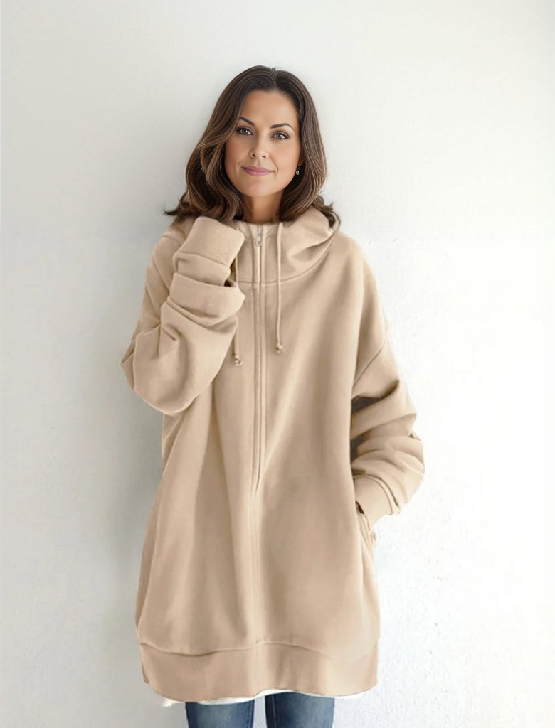 Frau in beigem Oversize-Hoodie vor weißem Hintergrund, lächelt. Modetrend, lässiger Stil, bequeme Kleidung, Damenmode, Herbstoutfit.