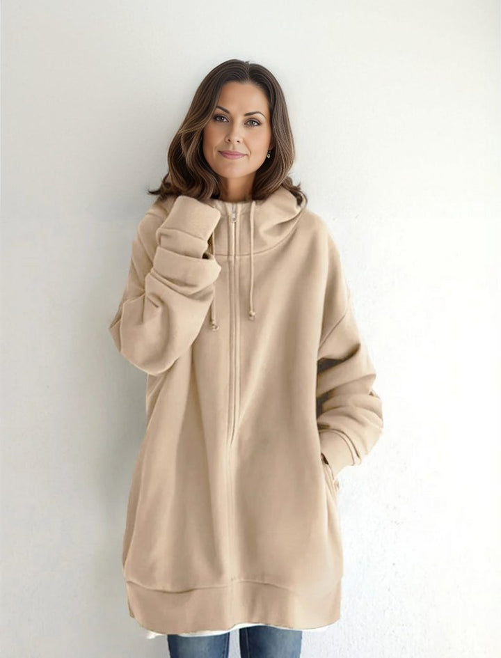 Frau in beigem Oversize-Hoodie vor weißem Hintergrund, lächelt. Modetrend, lässiger Stil, bequeme Kleidung, Damenmode, Herbstoutfit.