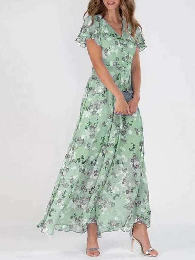 Frau in langem, grünem Blumenkleid mit kurzen Ärmeln und V-Ausschnitt, trägt silberne High Heels. Elegantes Sommeroutfit, modisch und feminin.