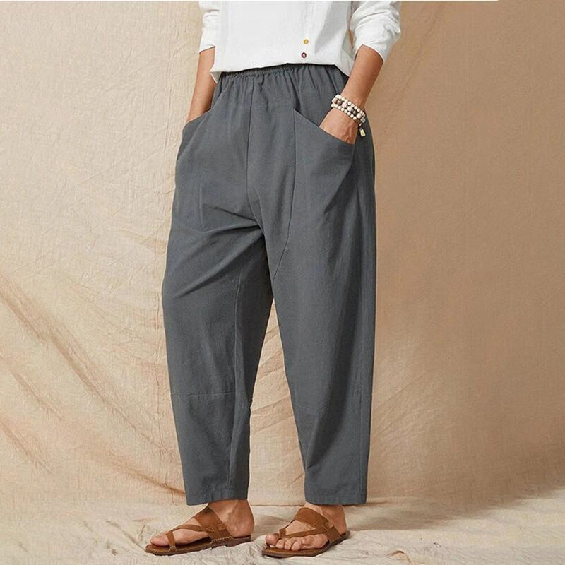 Person trägt graue, locker sitzende Haremshose mit Taschen, kombiniert mit weißem Oberteil und Sandalen. Bequeme Damenmode, lässiger Stil.