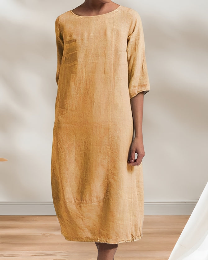 Frau in lockerem, knielangem, senfgelbem Leinenkleid vor neutralem Hintergrund. Minimalistisches Design, modisch, bequem, zeitlos.