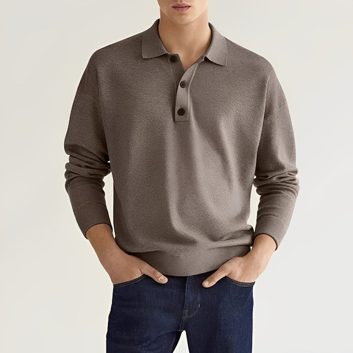 Junger Mann in grauem Poloshirt und blauer Jeans vor neutralem Hintergrund. Modetrend, Herrenbekleidung, lässiger Stil.