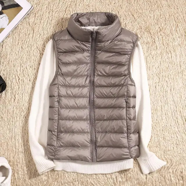 Graue Steppweste auf weißem Pullover, flach auf beigem Teppich liegend. Modische Winterbekleidung, ärmellose Jacke, warm und stilvoll.