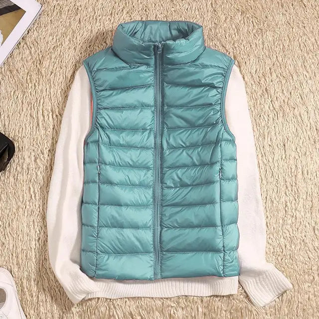 Türkise Steppweste auf weißem Pullover, flach auf beigem Teppich. Modische Damenbekleidung, Herbstmode, ärmellose Jacke, Outdoor-Bekleidung.