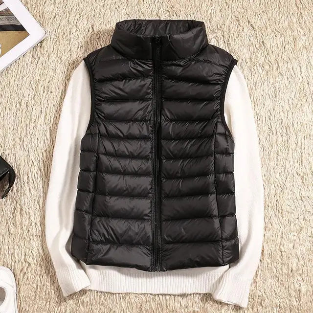 Schwarze Daunenweste auf weißem Pullover, flach auf beigem Teppich. Modetrend, Winterbekleidung, warme Outdoor-Weste, stilvolle Damenmode.