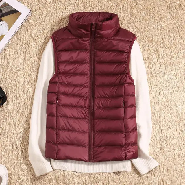 Bordeauxrote Steppweste auf cremefarbenem Pullover, flauschiger Teppich. Modische Winterbekleidung, ärmellose Jacke, warme Daunenweste.