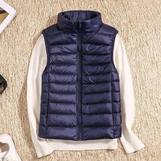 Dunkelblaue Steppweste auf weißem Pullover, beige Teppichhintergrund. Modische Winterbekleidung, ärmellose Jacke, warme Outdoor-Weste.