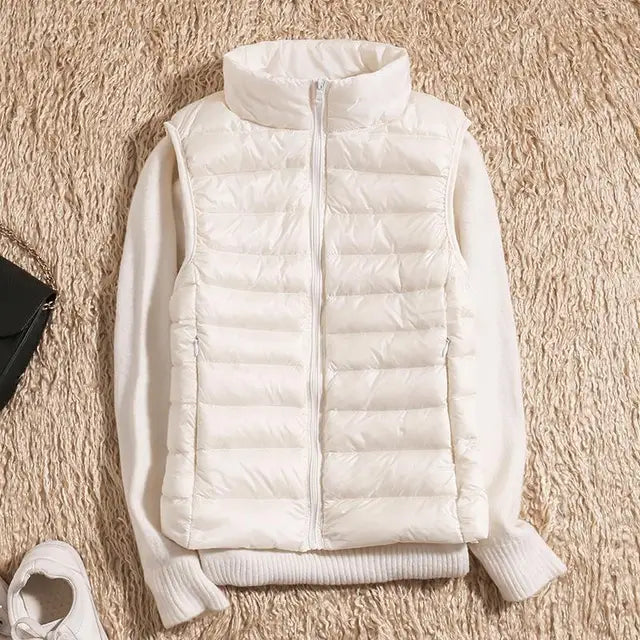 Weiße Daunenweste auf beigem Teppich, kombiniert mit weißem Pullover. Modische Winterbekleidung, warm und stilvoll. Ideal für kalte Tage.