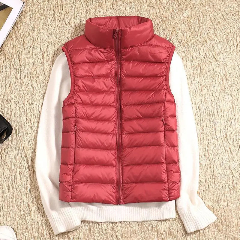 Rote Daunenweste auf weißem Pullover, flach auf beigem Teppich. Modische Winterbekleidung, warm, ärmellos, Reißverschluss, gesteppte Weste.