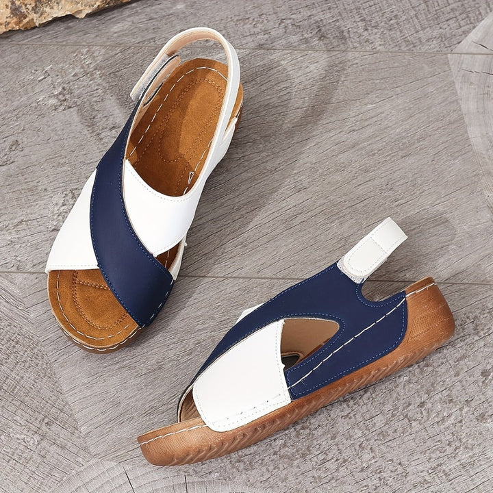 Damen-Sandalen mit blau-weißen Riemen, ergonomischem Fußbett und rutschfester Sohle auf grauem Holzboden. Bequeme Sommerschuhe.