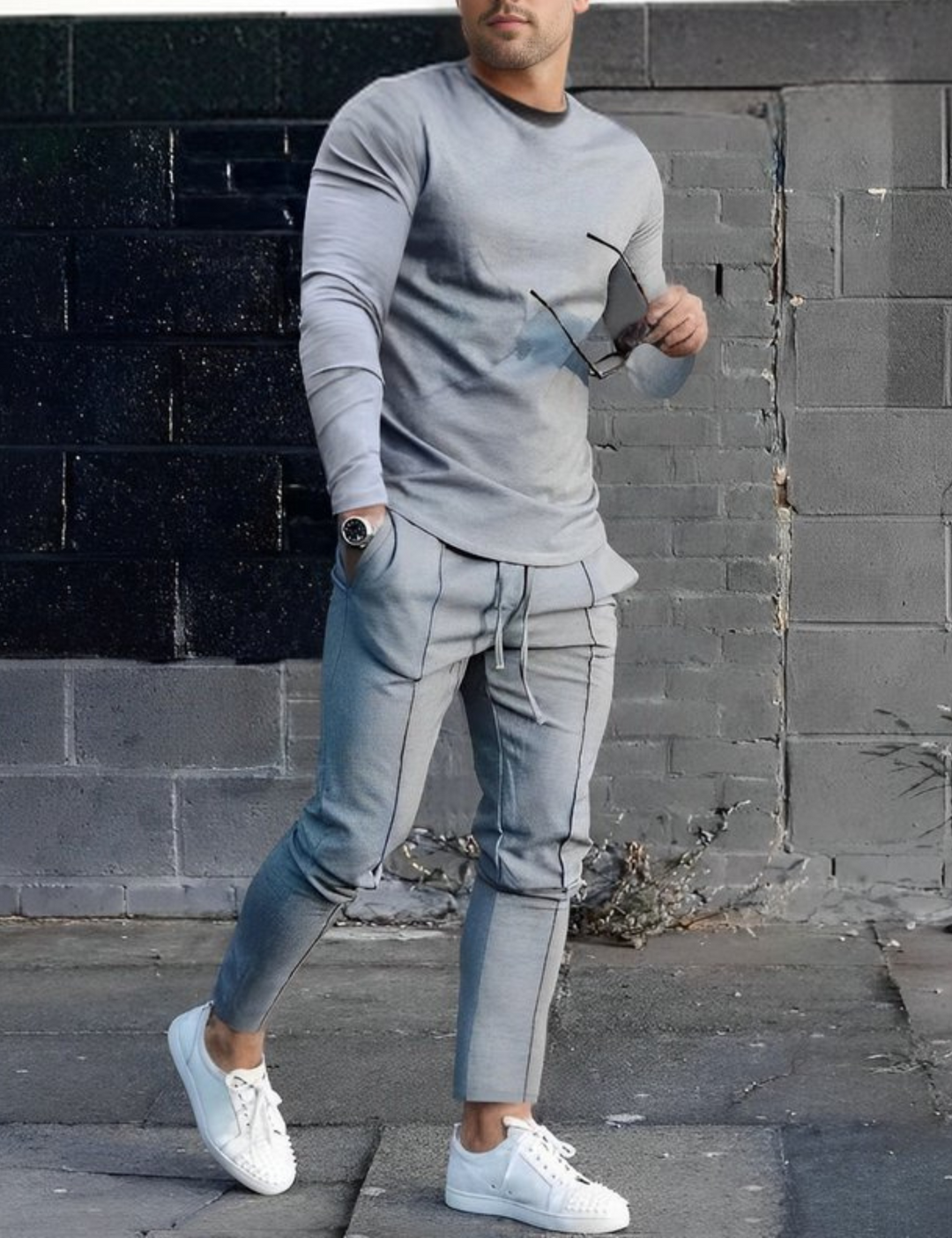 Grauer Herren-Sportanzug, lässig, mit langen Ärmeln und Kordelzughose, kombiniert mit weißen Sneakers. Urbaner Stil, modisch, bequem.