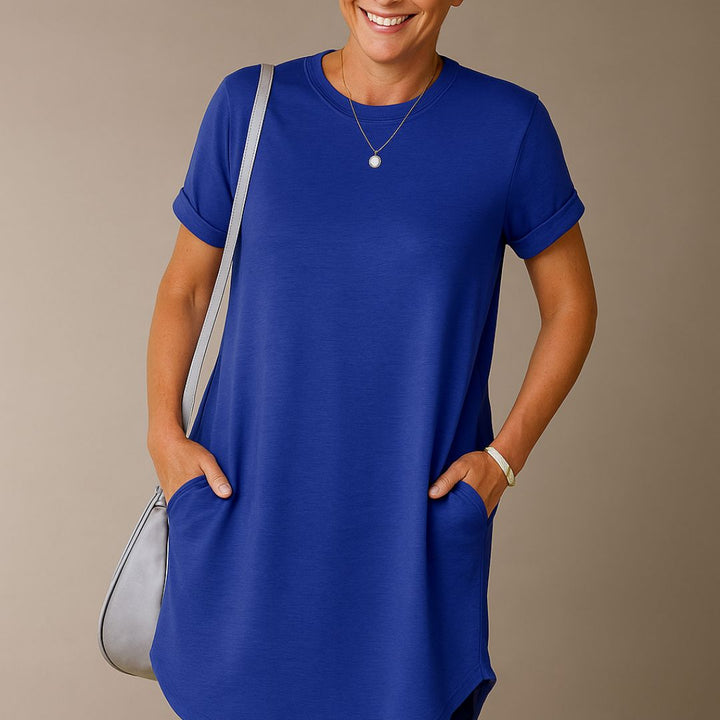 Frau in blauem T-Shirt-Kleid mit Taschen, lächelnd, trägt eine graue Umhängetasche. Mode, Damenbekleidung, lässiger Stil.