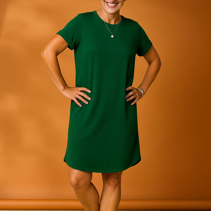 Grünes Damenkleid vor orangefarbenem Hintergrund, lächelnde Frau, modisches Freizeitoutfit, Sommerkleid, kurzärmelig, knielang, elegantes Design.