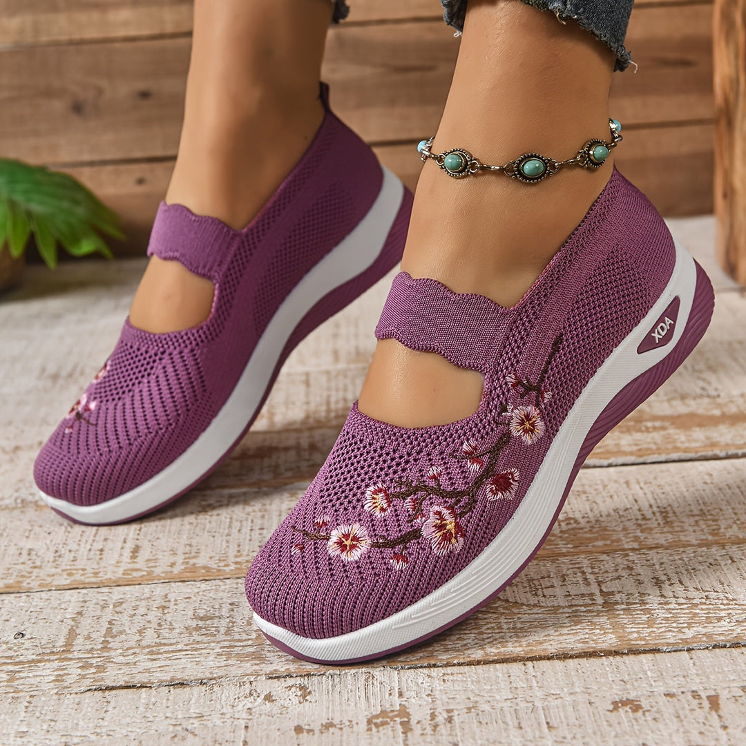 Lila Damen-Sneaker mit Blumenstickerei, atmungsaktivem Mesh-Obermaterial und Keilabsatz auf Holzboden. Modische Freizeitschuhe für den Sommer.
