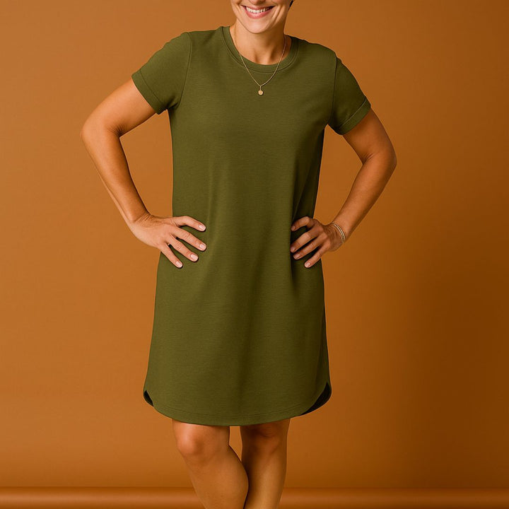 Frau in olivgrünem T-Shirt-Kleid vor braunem Hintergrund, lächelnd, mit Händen in der Hüfte. Modetrend, lässiges Damenoutfit, Sommerkleid.