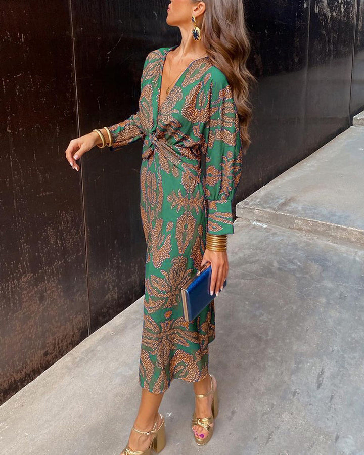 Frau in grünem, gemustertem Maxikleid mit goldenen Accessoires und blauer Clutch. Elegante Mode, Streetstyle, Herbsttrends.