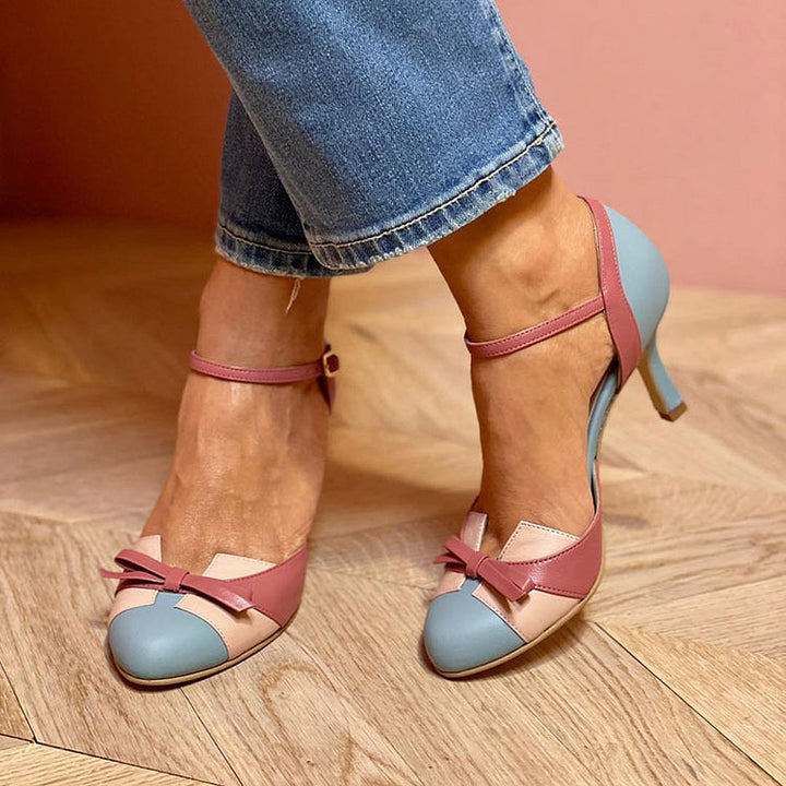 Frau trägt elegante, mehrfarbige High Heels mit Schleifen-Detail, kombiniert mit blauer Jeans. Modische Damenschuhe, stilvoller Look.