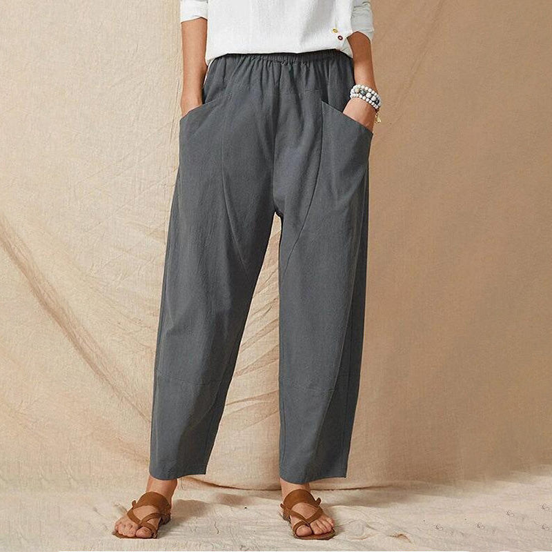 Frau in grauer, lockerer Leinenhose mit Taschen, weißem Oberteil und Sandalen. Modetrend, bequeme Damenbekleidung, lässiger Stil.