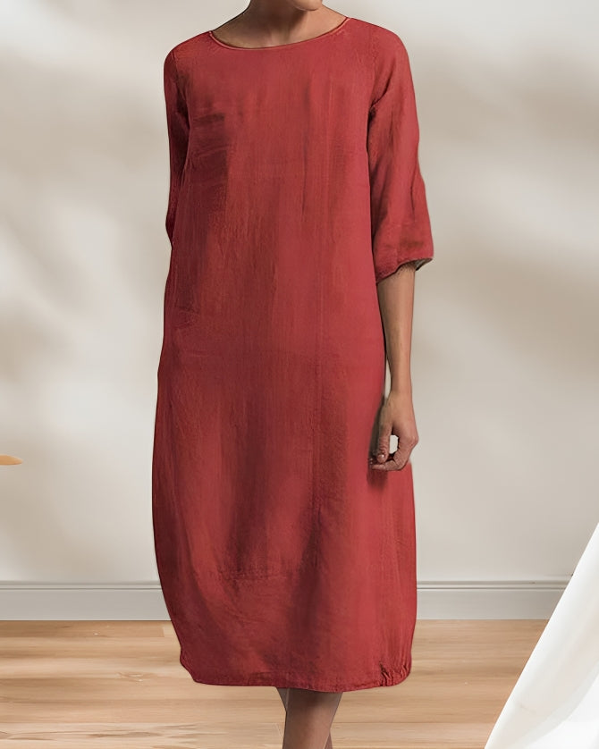 Frau in rotem Leinenkleid, knielang, mit 3/4-Ärmeln, steht in minimalistischem Raum. Elegantes, schlichtes Design, ideal für Sommermode.