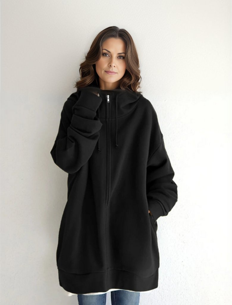 Eine Frau in einem übergroßen schwarzen Hoodie mit Reißverschluss und Kapuze, lässig vor einer weißen Wand stehend. Mode, Streetwear, Damenbekleidung.
