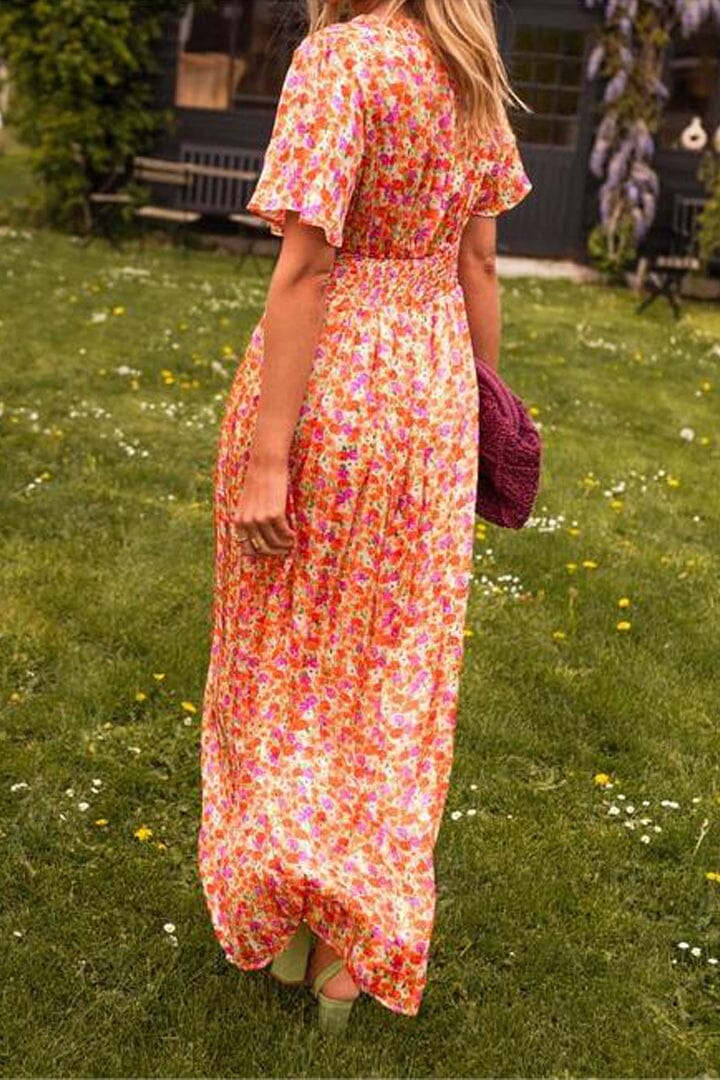 Frau in langem, geblümtem Sommerkleid auf Wiese, hält lila Tasche. Perfekt für Mode, Sommerkleider, Outdoor-Stil.