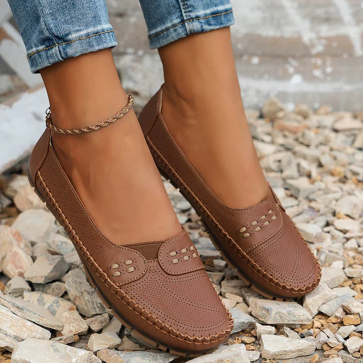 Braune Damen-Loafer aus Leder auf Kieselsteinen, modisch und bequem, ideal für Freizeit und Alltag, kombiniert mit blauen Jeans.