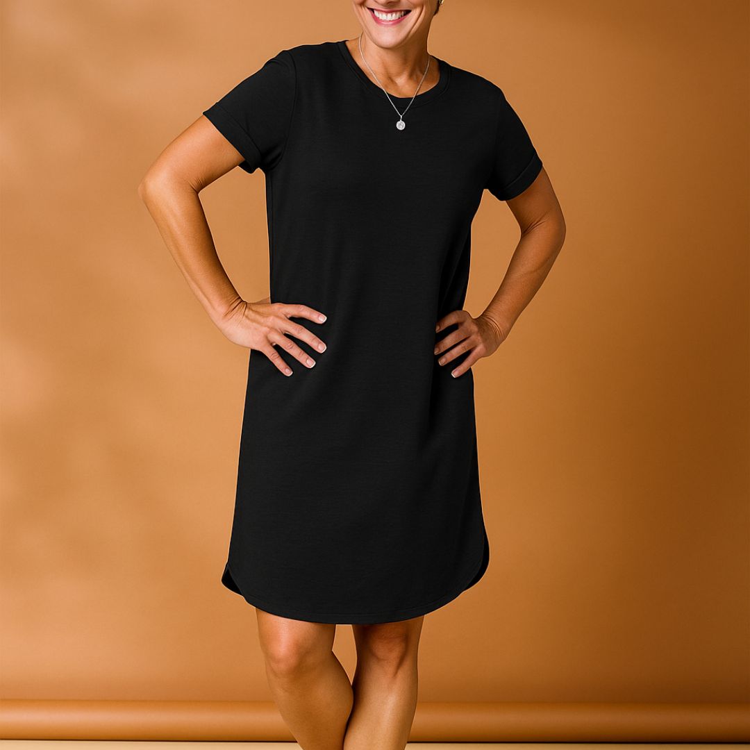 Frau in schwarzem T-Shirt-Kleid vor braunem Hintergrund, lächelnd, mit Händen in der Hüfte. Modetrend, lässiges Damenoutfit, Sommerkleidung.