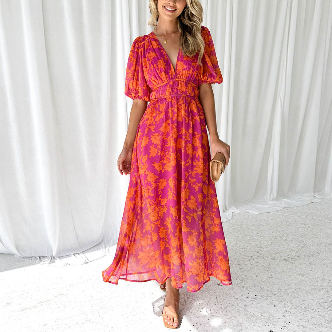 Frau in langem, geblümtem Sommerkleid in Pink und Orange, steht vor weißen Vorhängen. Elegantes Design, modische Kleidung, Sommermode.