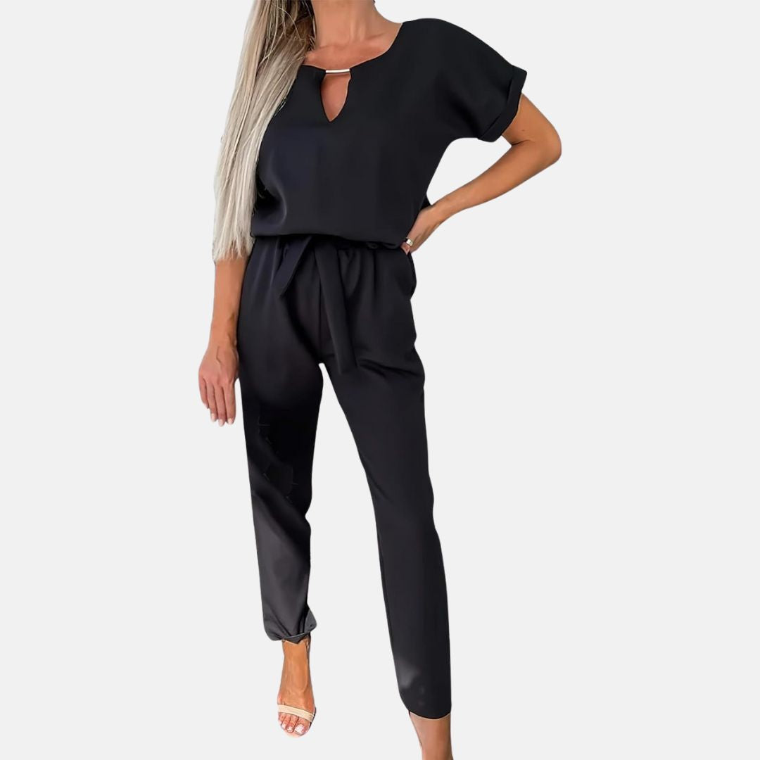 Frau in schwarzem Jumpsuit mit kurzen Ärmeln und V-Ausschnitt, modisch elegant, stehend vor weißem Hintergrund, Sommermode Damenbekleidung.